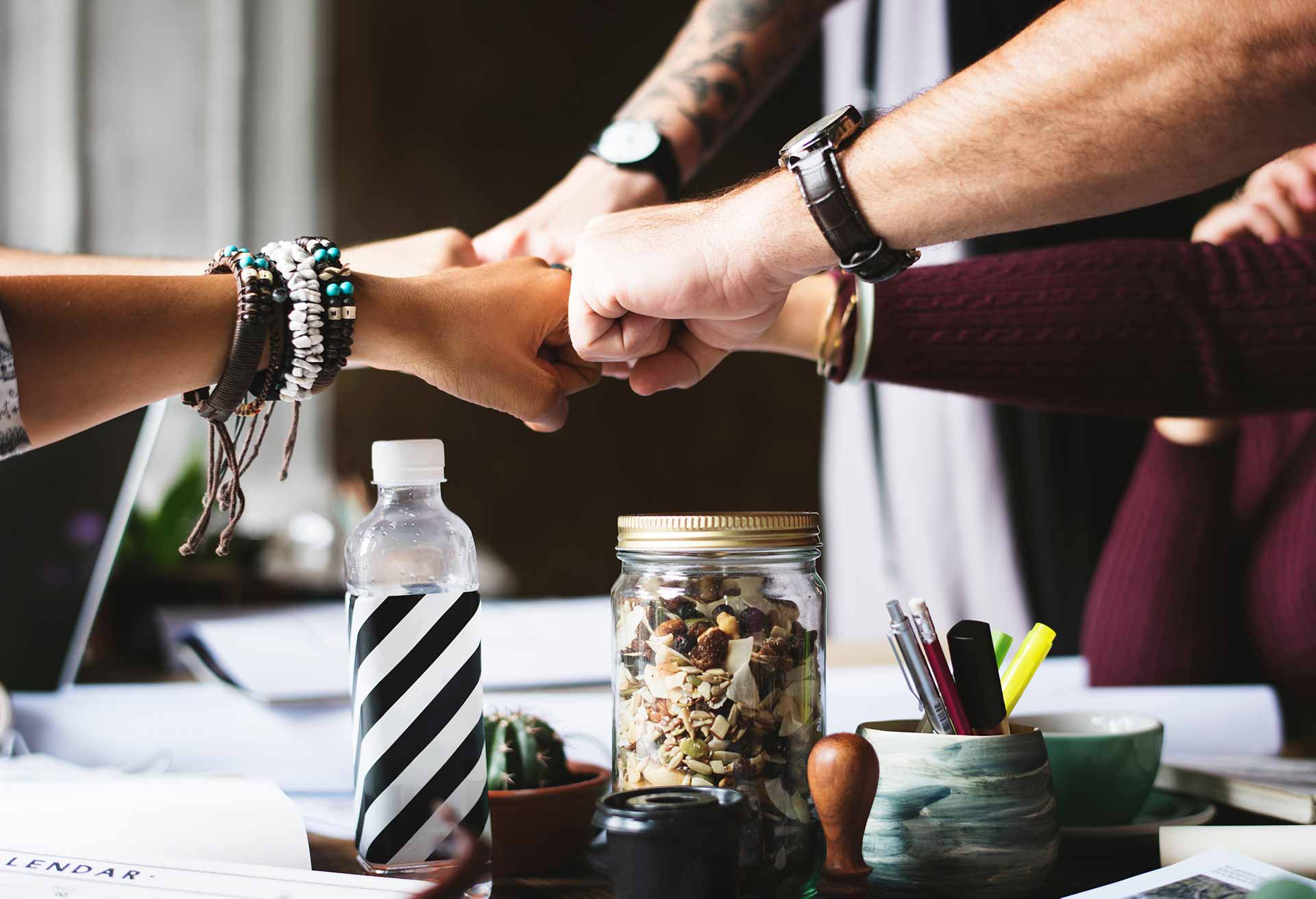 Five colleagues join fists together over a work table like a sports team