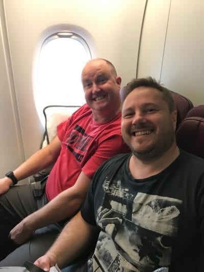 two men sitting in an airport, posing and smiling for the camera