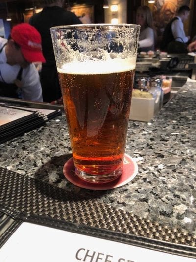 a pint glass of ale, with condensation dripping down the glass, sitting on a granite table in a busy restaurant