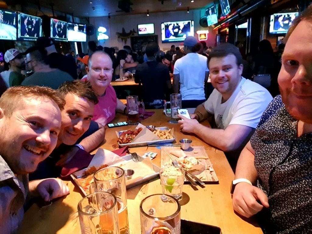 group of men around table in busy sports bar with many tv screens